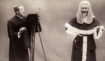 Een man in een soutane richt de lens van zijn camera op een man gekleed als een paus door Rotary Photographic Co Ltd