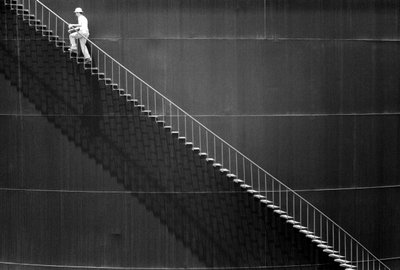 Man klimt trappen op de zijkant van een olietank door Ted Spiegel
