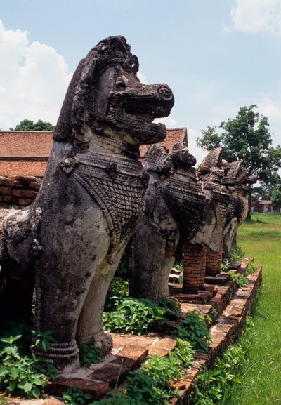 Leeuwachtige stenen bewakersfiguren gebouwd rond de basis van de stupa door Thai School