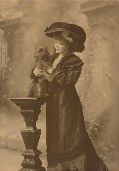 [Sarah Bernhardt staat in een studio en houdt een klein zwart hondje vast op een sierlijk, gebeeldhouwd houten voetstuk]. door Theodore C. Marceau