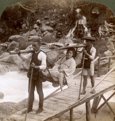 Japanse vrouw in een yamakago bergstoel die de stromende Daiya rivier bij Nikko, Japan, oversteekt door Underwood and Underwood