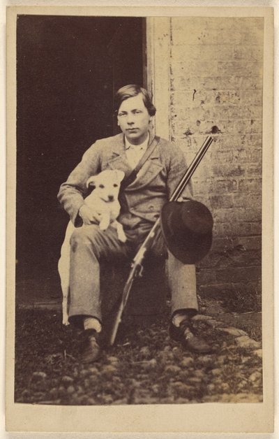[Man zittend met een witte hond, een geweer en hoed leunend op zijn been]. door Unknown artist