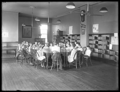 Kinderen luisteren naar een vrouw in de leeszaal van een niet-geïdentificeerde vestiging van de Queens Borough Public Library, c.1910 door William Davis Hassler