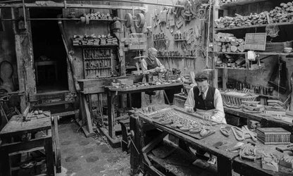 Ambachtslieden aan een werkbank in een werkplaats die kleine houten voorwerpen maken
