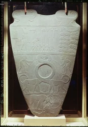 De Narmer-palet: ceremoniële palet met koning Narmer, met de rode kroon van Beneden-Egypte, die gebonden en onthoofde gevangenen inspecteert, ook een paar gigantische, langnek katten, gevonden in Hieraconpolis