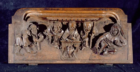 Een misericord die een academicus toont, zittend aan een paneelbureau, die een vermaning geeft aan een knielende boeteling, New College Chapel, Oxford, laat 14e eeuw (hout)