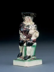 Dick Whittington jug, gemodelleerd zittend op een hoge stoel, zijn kat vasthoudend, gespat in bruine, groene en zwarte kleding, een gemodelleerd schild aan zijn zijde, c.1790
