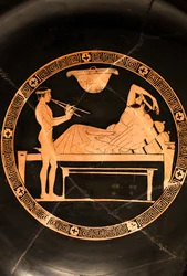 Beker: symposiast en jonge slaaf die de dubbele aulos speelt (Rood-figuur keramiek,)
