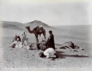 Egyptische kameeldrijvers tijdens een pauze in de woestijn. Op de voorgrond lijken twee leden van de kleine groep te bidden