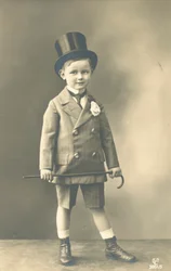 Jongen in dubbelknoopspak, met hoge hoed en wandelstok