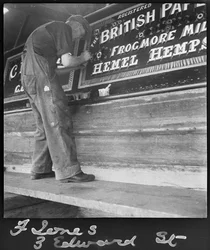 Frank Jones, aan het werk met het schilderen van het naampaneel op een binnenschip, 20e eeuw (foto)