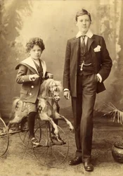 Jonge jongen op zijn paard gemonteerd als een driewieler, zijn oudere broer ernaast, 1880s
