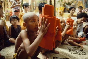 Een jonge jongen met geschoren hoofd ontvangt zijn monnikskleding. Mandalay, Birma