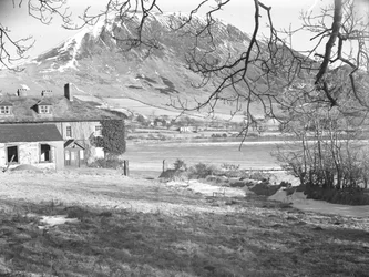 Het Anglers Hotel in Ennerdale met bomen op de voorgrond en bevroren meer en besneeuwde heuvels daarachter