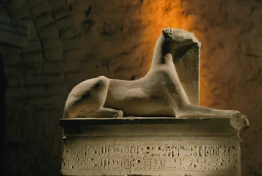 Kalkstenen beeld van de jakhalsgod Anubis geknield op een basis in de vorm van een sarcofaag, 2002