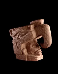 Precolumbiaanse kunst, Mayabeschaving, preklassieke periode: stenen sculptuur van het hoofd van een man dat oprijst uit de muil van een zoömorfe god die op de hemelvogel lijkt. 38 x 46 cm. Guatemala, Museo Nacional de Arqueología y Etnología