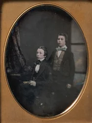 Twee jonge mannen in strikjes, een zittend met een boek, een staand
