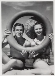 Man en vrouw die door een rubberen ring op het strand kijken, circa 1935