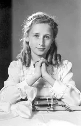 Christelijk meisje met gevouwen handen in gebedspositie met bijbel, rozenkrans en kaars (foto van communie). Fotografie rond 1932