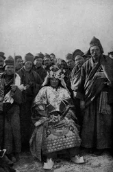 Tibet. Tovenaar in vol ornaat en een bewonderende groep monniken. 1920