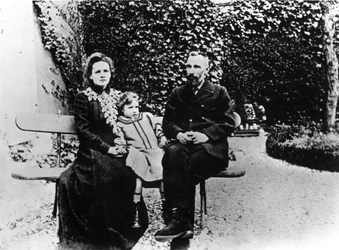 Pierre (1859-1906) en Marie Curie (1867-1934) zittend op een bankje in een tuin.