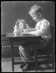 William Gray Hassler zittend aan een kleine tafel etend een kom Quaker gepofte rijst, ca.1912